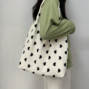 Close-up of heart print canvas tote bag with wide shoulder strap on green knit sweater