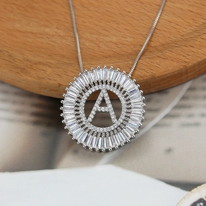 Close-up of a silver letter A pendant with baguette-cut zircon and box chain on wood