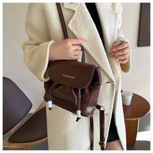 Detail eines Retro-Rucksacks aus Leder und Karo mit Kordelzug, getragen zu einem Wintermantel
