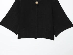 Macro detail of black knit texture and a large polished gold round button on the cardigan