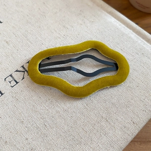 Close-up of irregular wave-shaped velvet hair clip in olive green on a fabric book