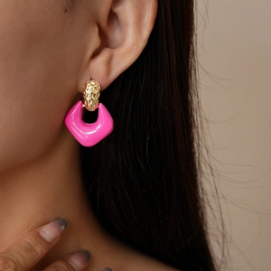 Detail view of a model wearing a pink geometric drop earring with hammered gold texture
