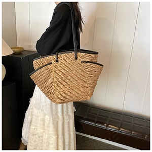 Detail of a large straw tote bag with black leather shoulder straps and woven texture