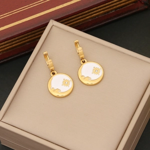 Primo piano di orecchini dorati con dischi di smalto bianco e delicati motivi floreali d'oro