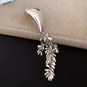Macro shot of silver metal brooch featuring flowing liquid shapes and layered leaf tassels