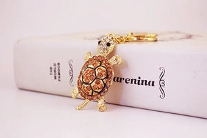 Detailed macro shot of golden alloy turtle keychain with orange rhinestones on white book
