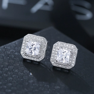 Macro shot of silver square zircon stud earrings with sparkling halo setting on black texture