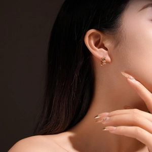 Close-up of golden geometric rhombus earrings with sparkling crystals on model ear