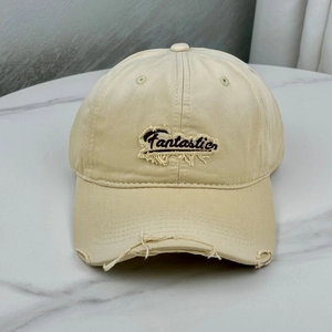 Detail of vintage beige baseball cap with Fantastic embroidery and distressed ripped brim