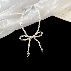 Gros plan du pendentif nœud métallique avec des perles carrées sur un collier argenté