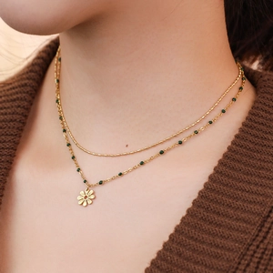 Detail of layered gold stainless steel necklace featuring green beads and floral pendant
