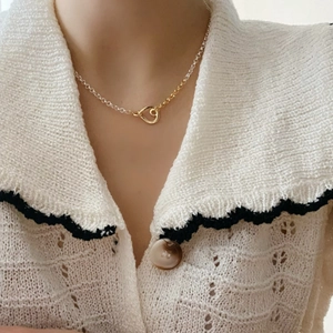 Detail of a minimalist two-tone silver and gold heart knot necklace on a model's collarbone