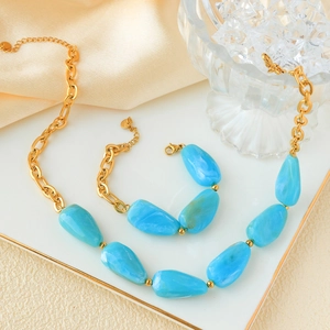 Close-up of gold chain necklace and bracelet set with sky blue marble stones on white board