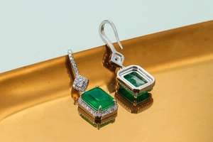 Elegant emerald-cut green stone earrings with halo diamonds on a golden tray