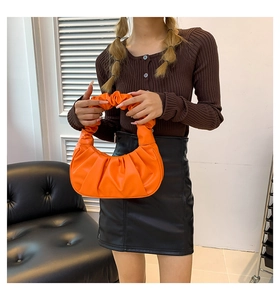 Detail of orange pleated leather dumpling bag shown on a model in an indoor setting