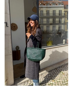 Detail of dark green woven leather tote bag carried by a model in a city street