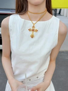 Gros plan d'un collier doré à deux rangs avec pendentif croix et gemmes oranges