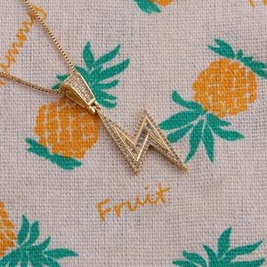 Macro shot of gold plated lightning bolt pendant with zircon stones on a box chain