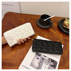 Close-up of black and white quilted long wallets on a wooden table with lifestyle props