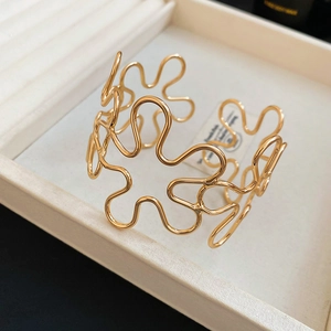 Detail of a wavy gold hollow flower cuff bracelet resting inside a beige jewelry box