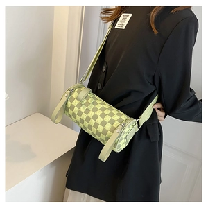 Detail of checkered cylinder crossbody bag featuring wide canvas strap and pale green pattern