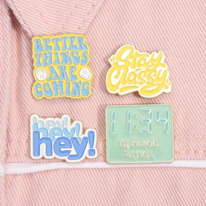Macro detail of four enamel motivational pins on pink denim, featuring vibrant metal alloy