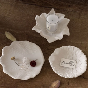 Three-piece set of white leaf and floral shaped ceramic decorative trays on a wooden table