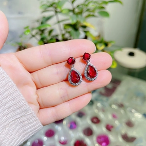 Detailed view of red pear-cut zircon earrings with white crystal halo held by hand