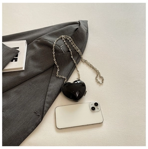 Flat lay of a black heart-shaped crossbody bag with faceted gemstone finish and silver chain