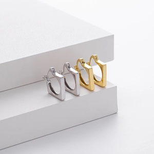 Close-up of square geometric hoop earrings in gold and silver finishes on a white stand