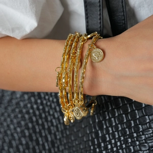 Detail of gold layered bracelets featuring hammered textures and coin pendants on wrist