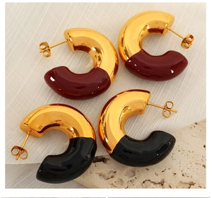 Detail of C-shaped earrings in gold with burgundy and black enamel on textured stone