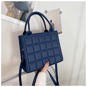 Detail of dark blue quilted handbag held by hand with focus on texture and strap
