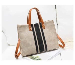 Detail of beige canvas tote bag with black vertical stripes and brown leather handles