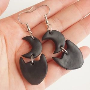 Detail of handmade black clay moon and cat head earrings held in hand for scale
