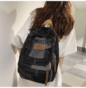 Back view of a black denim patchwork backpack with brown leather tags and white stitching
