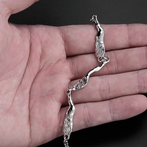 Irregular textured silver metal link bracelet held on palm with a black background
