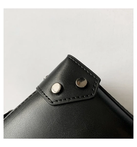 Macro detail of black leather crossbody bag featuring silver rivets and contrast stitching