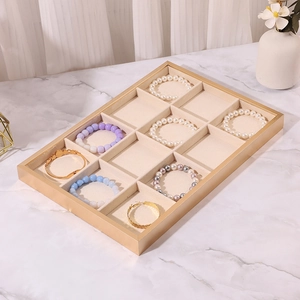 Detail of 12-slot gold metal jewelry tray with beige velvet lining on marble