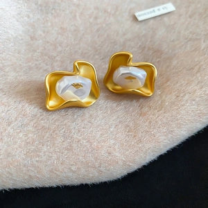 Close-up of matte gold flower petal earrings with pearl centers on soft beige fabric