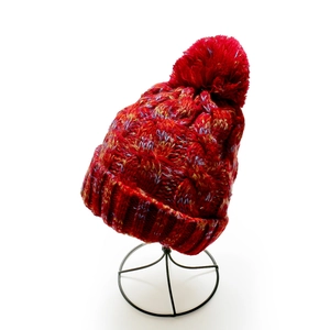 Close-up of red knit beanie featuring thick mixed yarn texture and a large matching pom-pom