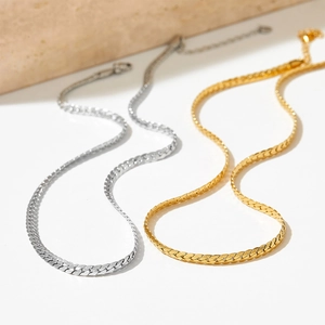 Polished silver and gold Cuban link chain necklaces on a minimalist stone display