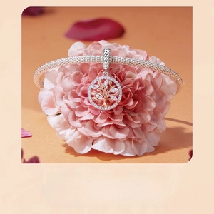 Rose gold tree of life charm with clear zircons on silver bracelet over pink flowers