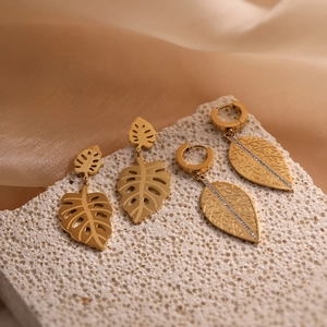 Orecchini a foglia d'oro con design monstera e diamanti su una base di pietra