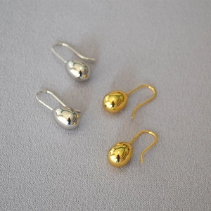 Macro detail of drop earrings in gold and silver finish on textured fabric