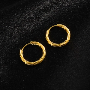 Close-up of golden twist hoop earrings on black silk background with a textured finish