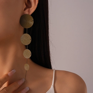 Close-up of golden geometric earrings with tiered spiral discs worn by a female model