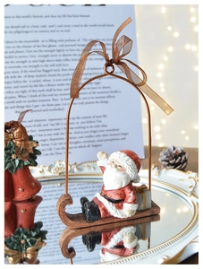 Detailed close-up of a Santa figurine on a wooden sleigh with a red bell and pine decor