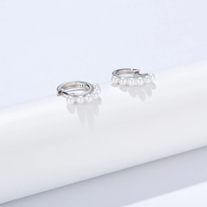 Macro detail of silver hoop earrings with round white pearls against a white background