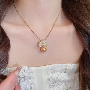 Close-up of gold-plated clover pendant with shimmering zircons and round gold pearl